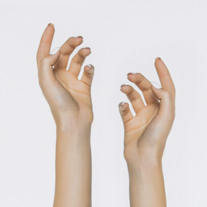 Two light-skinned hands reach upward with fingers curved against a pale background.
