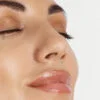 Close-up of a woman's face with closed eyes, smooth skin, and glossy pink lips.