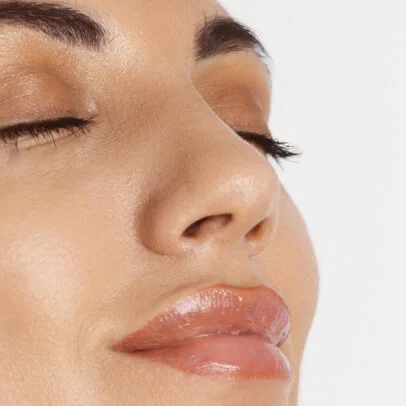 Close-up of a woman's face with closed eyes, smooth skin, and glossy pink lips.