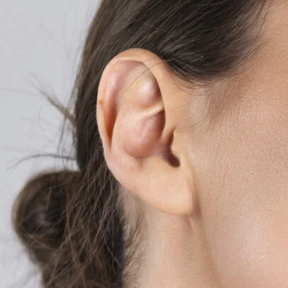 Close-up of a human ear with surrounding skin and hair tied back.