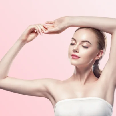 Woman with eyes closed, arms raised above her head in a relaxed pose against a pink gradient background, wearing a white strapless top.