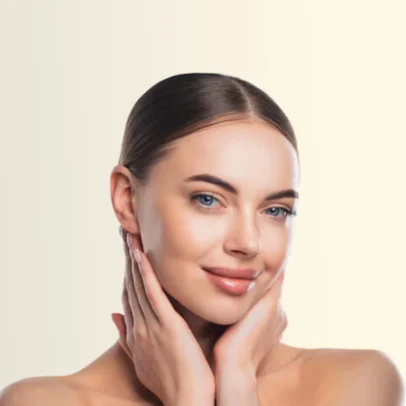 Portrait of a smiling woman gently cupping her face with both hands, showcasing clear skin against a pale background