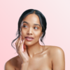 Portrait of a woman with smooth skin touching her cheek against a soft pink background, studio lighting.