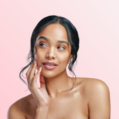 Portrait of a woman with smooth skin touching her cheek against a soft pink background, studio lighting.