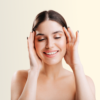 Smiling young woman with eyes closed, hands cupping her face against a pale beige background.