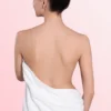 Back view of a woman with bare shoulders and a white towel wrapped around her waist against a pink gradient background.