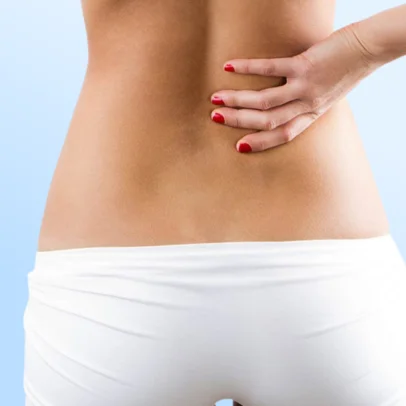 Close-up of a person's lower back with a hand pressed on the area, wearing white underwear against a light blue background.