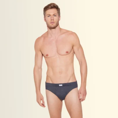 Male model wearing dark gray briefs, standing facing the camera against a pale gradient background.