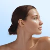 Profile of a woman with smooth skin and a low bun, looking to the right against a light blue gradient.