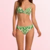 Woman wearing a green and white patterned bikini top and matching bottoms, standing against a pink background.
