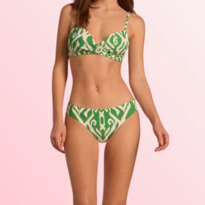 Woman wearing a green and white patterned bikini top and matching bottoms, standing against a pink background.