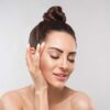 Close-up of a woman with a bun touching her cheek with her hand, eyes closed.