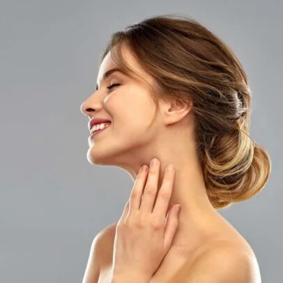 Woman with a neat bun, smiling softly, touching her neck with fingers.