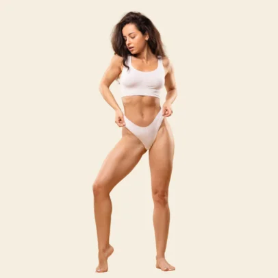 Woman in a white sports bra and high-cut underwear striking a dynamic pose against a pale beige background.