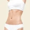 Toned midsection of a person wearing a white sports bra and white underwear against a light beige background.