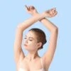 Woman stretching with arms crossed overhead, eyes closed, against a light blue background.