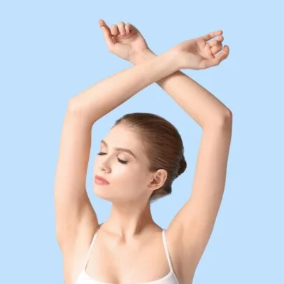 Woman stretching with arms crossed overhead, eyes closed, against a light blue background.
