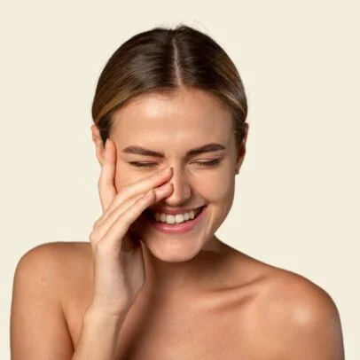 Woman smiling with eyes closed, pinching her nose with fingers in a playful pose.