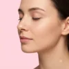 Close-up profile of a woman with smooth, even-toned skin and closed eyes against a pink background, highlighting skincare.