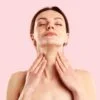 Woman with eyes closed, fingertips resting on her neck in a self-care pose against a pink background.