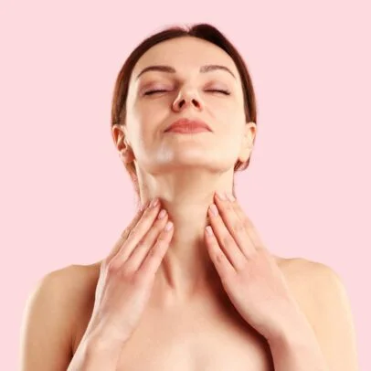 Woman with eyes closed, fingertips resting on her neck in a self-care pose against a pink background.
